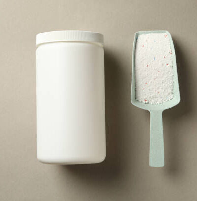 Plastic bottle and scoop with washing powder on gray background