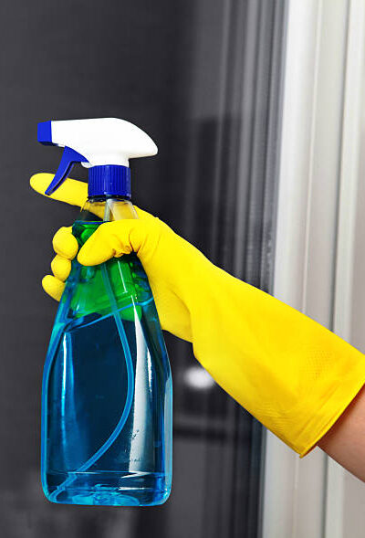 Hand in yellow glove holding spray for cleaning window